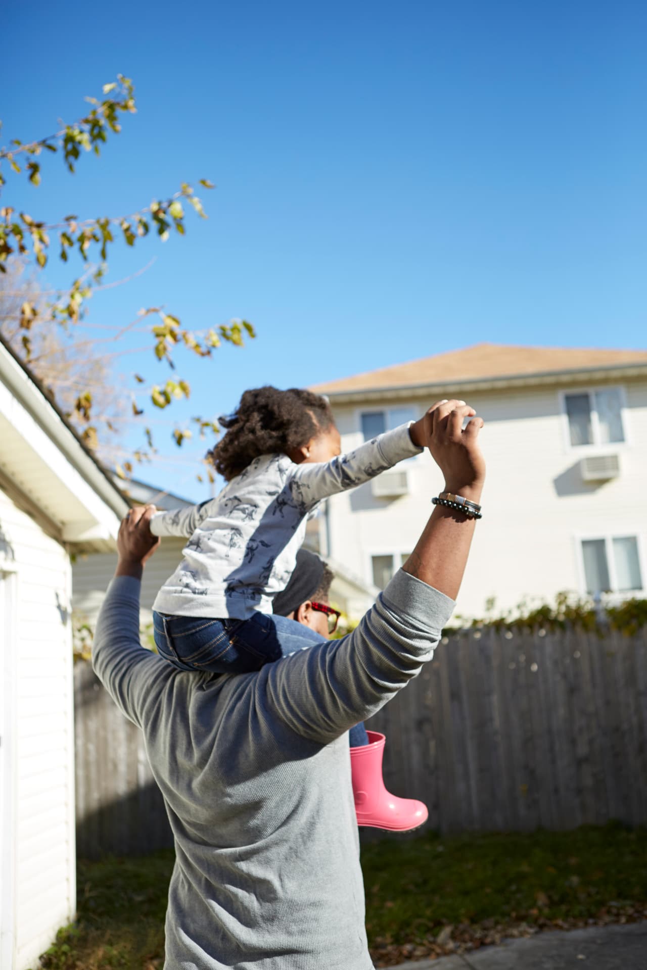 Father carrying his young daughter on his shoulders outside their home